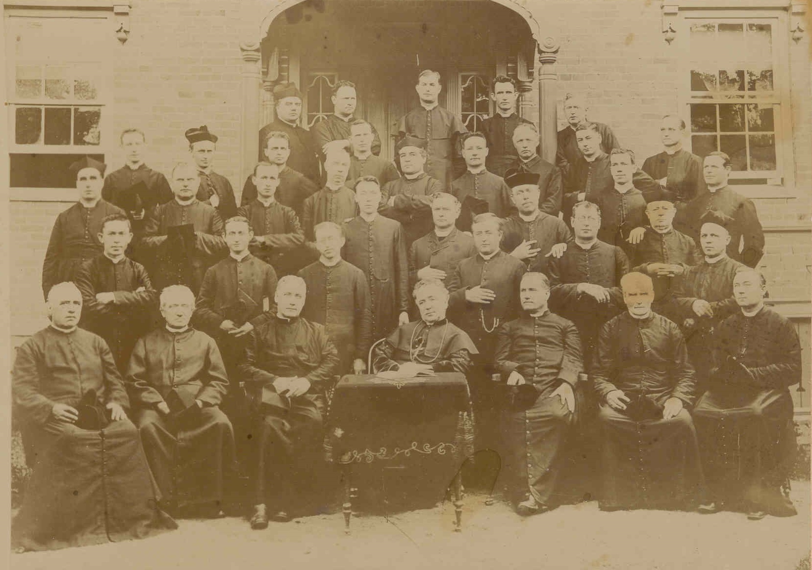 Sepia photograph depicting a group portrait of the clergy of the Diocese of Hamilton from 1894. There are five rows of clergy wearing cassocks and looking out at the viewer. The men in the front row are seated. Bishop Thomas Dowling is seated in the middle behind a small table.